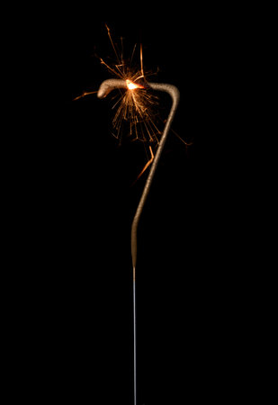 Burning golden sparkler in shape of number seven, digit 7, isolated on black background