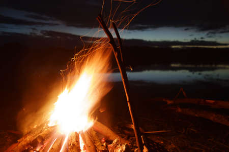 A fire and sparks on a long exposure at night near the water, a branch and a frying pan standing nearby for cookingの写真素材