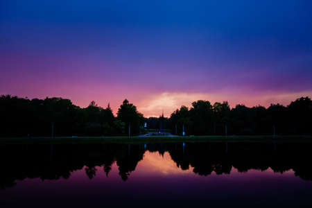 Blue purple sky at sunset, reflection of dark trees in the surface of the water.の写真素材