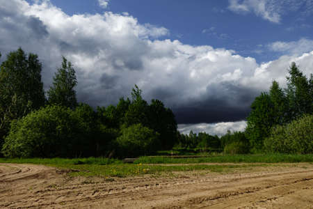 A dirt road and a forest, bushes, a gloomy sky with thundercloudsの写真素材