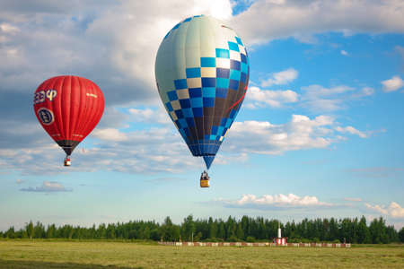 Two balloons, one red, the other blue, fly over the field at a low altitude, blue sky with cloudsのeditorial素材