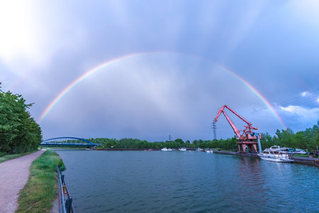 painting a rainbow in the blue sky above the river port with an old craneの写真素材