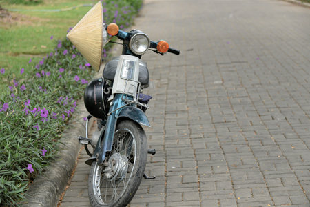 Ho Chi Minh City, 19 March 2021: Old, used, classic retro cub 50 motorcycle hanged with Asian cone hat and helmet park on concrete pavement block.のeditorial素材