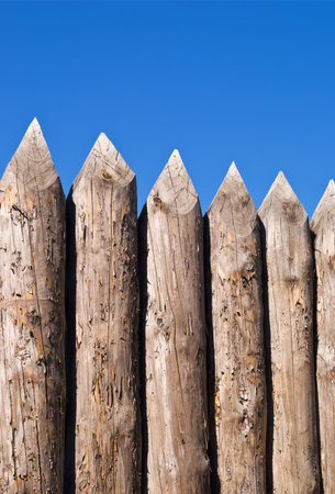 High wall of old wooden sharpened logs over blue sky