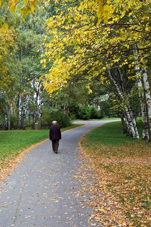 Autumn of life. Senior man walking along path in autumn parkの写真素材