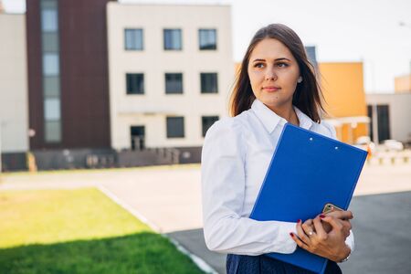 beautiful businesswoman with a folder in front of modern officeの写真素材
