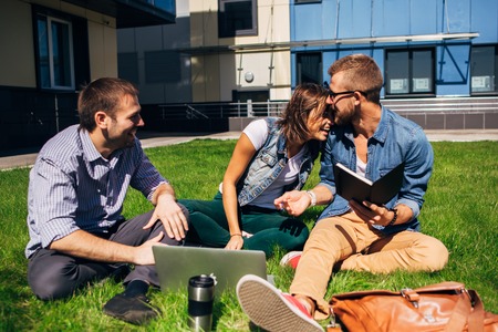 three students sitting on lawn at the universityの写真素材