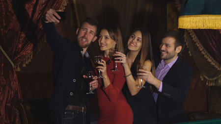 two beautiful young couples at the party take a selfie with glasses near pool tableの写真素材