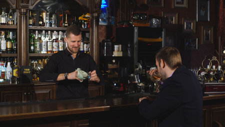Smiling attractive young barman wiping glasses and talking to young man in bar,the man came to relax...
