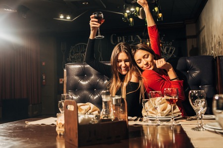 Pretty women talking and having fun inside restaurant,two young beautiful woman relaxing in the restaurant and drinking wineの写真素材