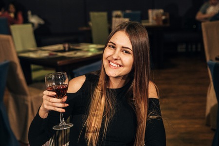 beautiful young woman tasting wine in a restaurant and smiling.happy womanの写真素材
