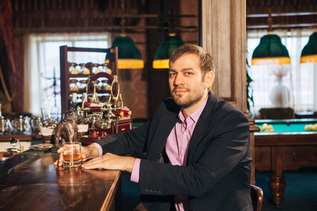 a man sits at the bar drinking whiskey and looking out the frame