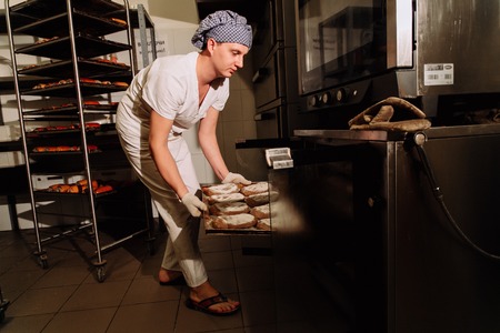 Baker taking a loaf of freshly baked bread from the oven in a modern bakery,the Baker taking fresh breadの写真素材