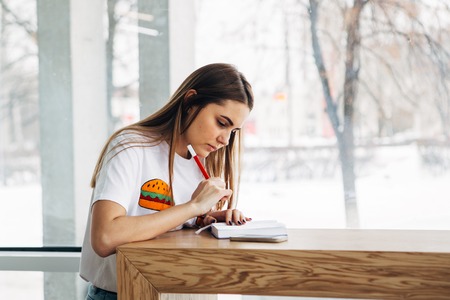 Young business woman sitting near window and recording data in notebookの写真素材