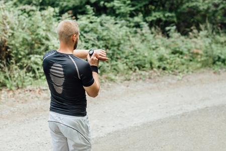 Rear view of a runner standing on a nature trail checking timeの写真素材