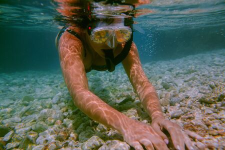 Woman snorkeling underwater. Female swimmer with diving mask and snorkel touching stones at bottom of shallow sea.の写真素材