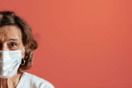 Elderly woman against pink background looking straight at camera wearing protection mask. Head and shoulders of old woman wearing face mask with copy space.の写真素材