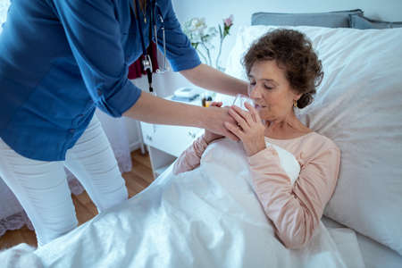 Nurse Helping Senior Patient Drink Water. Elderly Woman Lying in Bed Getting Glass of Water From Female Home Caregiver.の写真素材