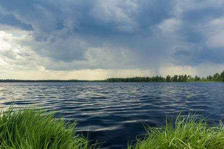 Dark sky on forest lake before storm rainの写真素材