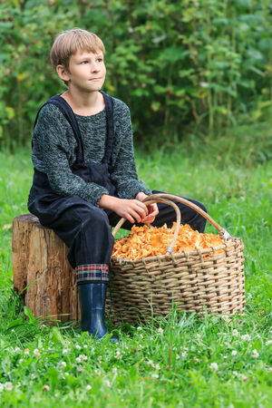 Ten years boy sitting with basket full of chanterellesの写真素材