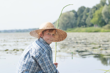 Angling teenage boy with handmade green twig fishing rod is looking back to cameraの写真素材