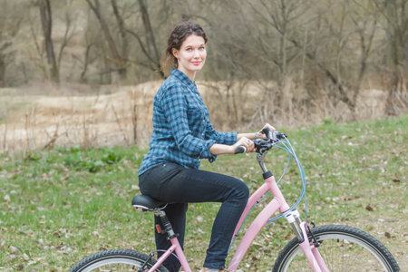 Cheerful brunette girl is cycling on dirt track in old park