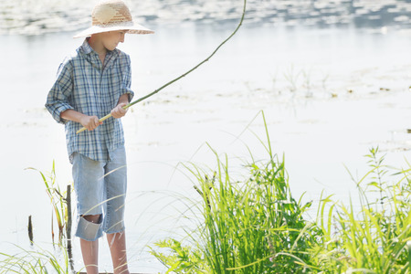 Angling teenage boy is looking at handmade green twig fishing rod in his armsの写真素材