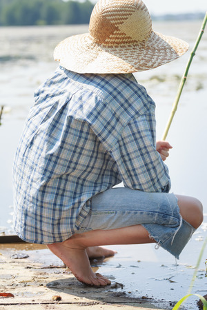 Sitting on wooden bridge barefoot young fisherman with fishing rodの写真素材
