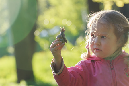 Three years old preschooler girl with short pigtails is holding edible snailの写真素材