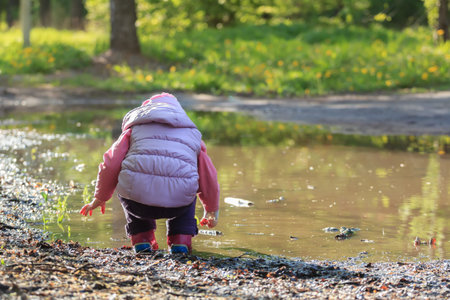 Toddler girl is looking for pebbles on big summer puddle bank