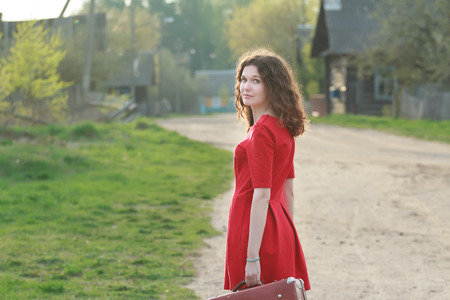 Young woman in feminine red dress is looking over her shoulder during her vintage travelの写真素材