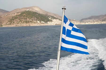 Greek national flag at sea waves and lonely island backgroundの写真素材