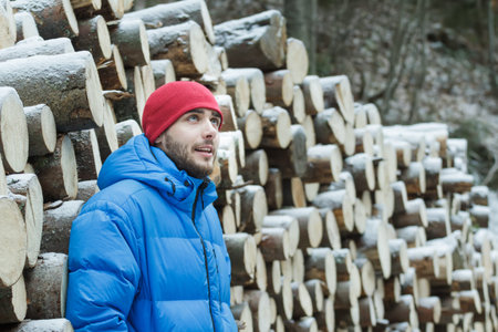 Resting woodcutter at wall of cut firewood background outdoors in winter mountain conifer forest