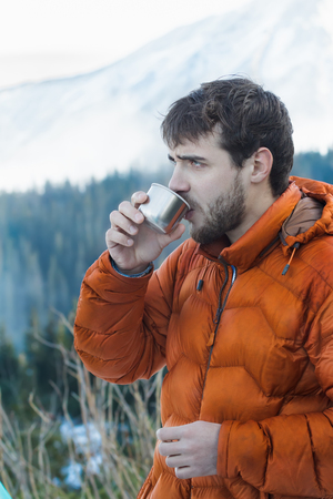 Portrait of resting mountaineer with hot drink metal vacuum flask at snowy winter mountains backgroundの写真素材