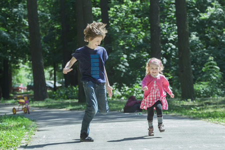 Laughing sibling children are playing tag and running on park asphalt footpathの写真素材