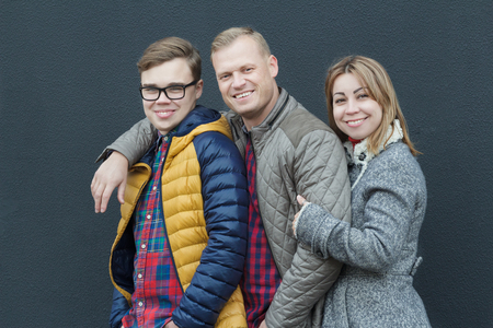 Family of three embracing people standing at black building wall backgroundの写真素材