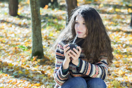 Young woman in knitted snowflakes pattern woolen sweater is drinking hot yerba mateの写真素材
