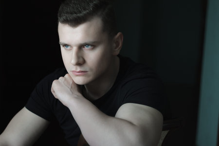 Young man with hand on shoulder low-key lighting indoor dark portraitの写真素材