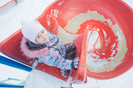 Winter activity of little girl on red spiral plastic playground slideの写真素材