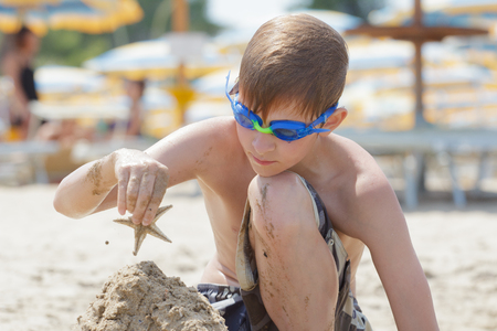 Concentrated beach boy is building sand castle with starfish on topの写真素材