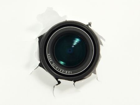 Digital camera object-glass uncovering from behind a paper wall, ready to take a snapshot.の写真素材