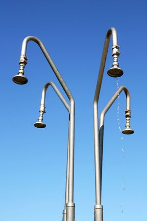 Four outdoor shower heads over deep blue and cloudless sky. Water leaking from one shower head. Green environment concept.の写真素材