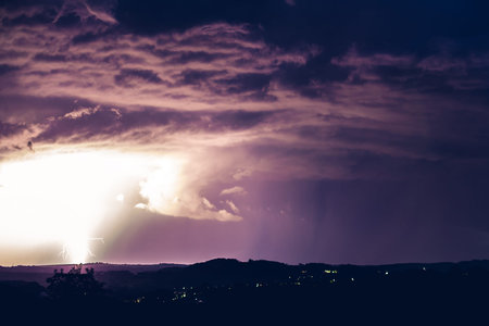 Night landscape on a background of thunderstorms. Rural silhouette and clouds with lightning flashes