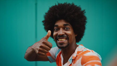 Close-up frontal portrait of cheerful young African American man wearing shirt smiling at the camera against light blue wall background. lifestyle concept.の写真素材