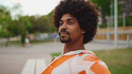 Close-up of young African American man wearing shirt sitting relaxed on park bench looking away. life style concept.の写真素材