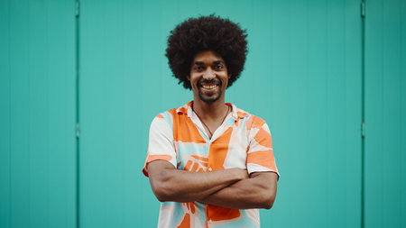 Close-up frontal portrait of cheerful young African American man wearing shirt smiling at the camera against light blue wall background. lifestyle concept.の写真素材