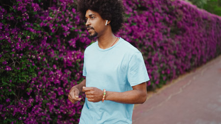 Closeup cheerful young African American man listening to music in wireless headphones and dancing on background wall covered with purple flowers. lifestyle concept.の写真素材