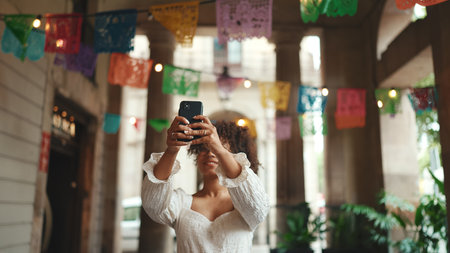 Closeup portrait of a young woman in glasses shots on smartphone downtown sightseeing. Positive woman using mobile phone outdoors in urban background.の写真素材