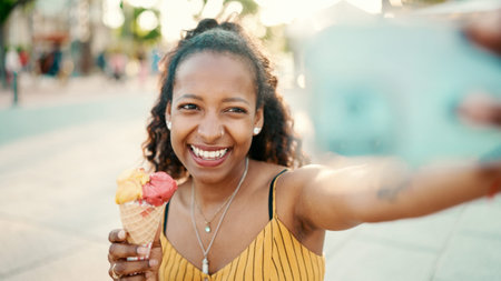 Closeup of smiling young woman with long curly hair with ice cream in her hands making a video call...