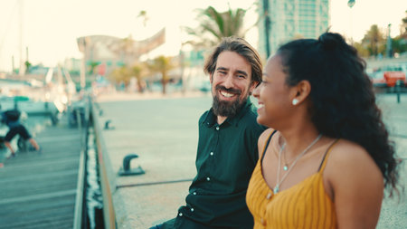 Close-up of happy interracial couple sitting in the port. Closeup, young family talking and smiling in front of passing yachtsの写真素材